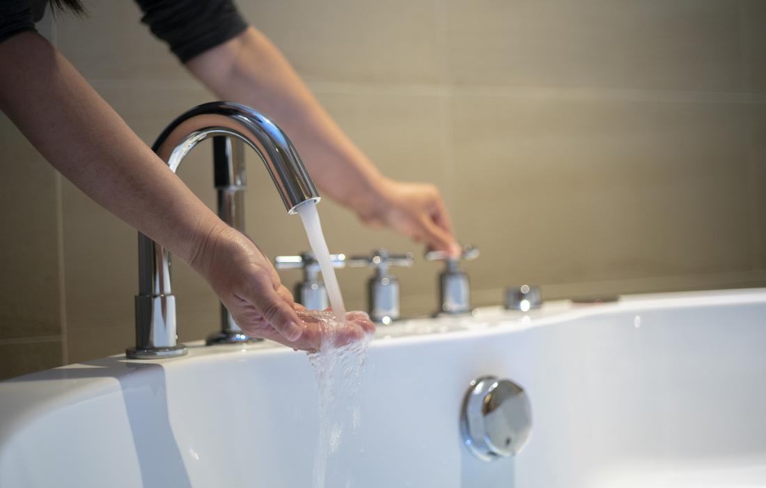 Person holding their hand under running water from a tap into a bath