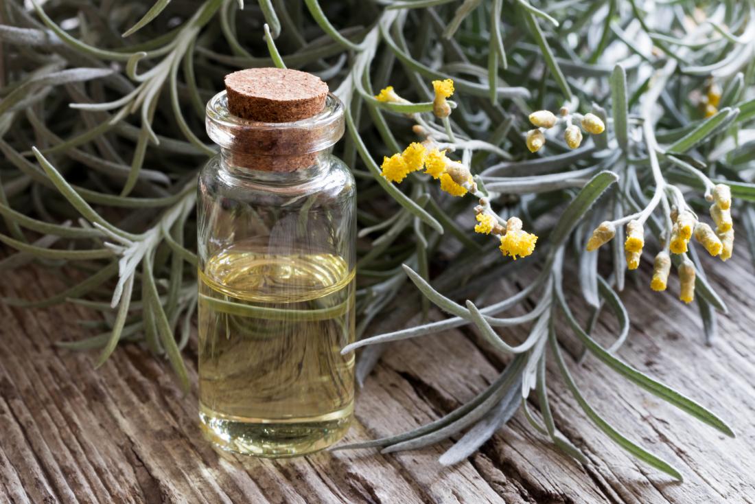 helichrysum essential oil in bottle next to plant on wooden table.