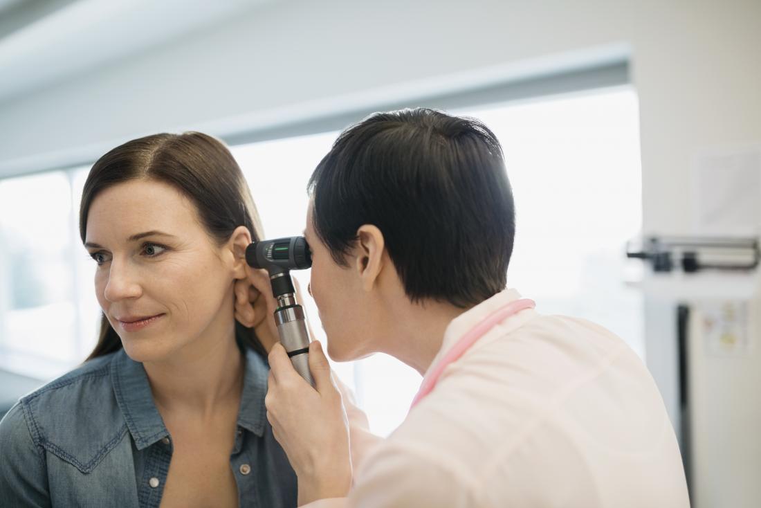 Woman having ear examined by doctor with otoscope