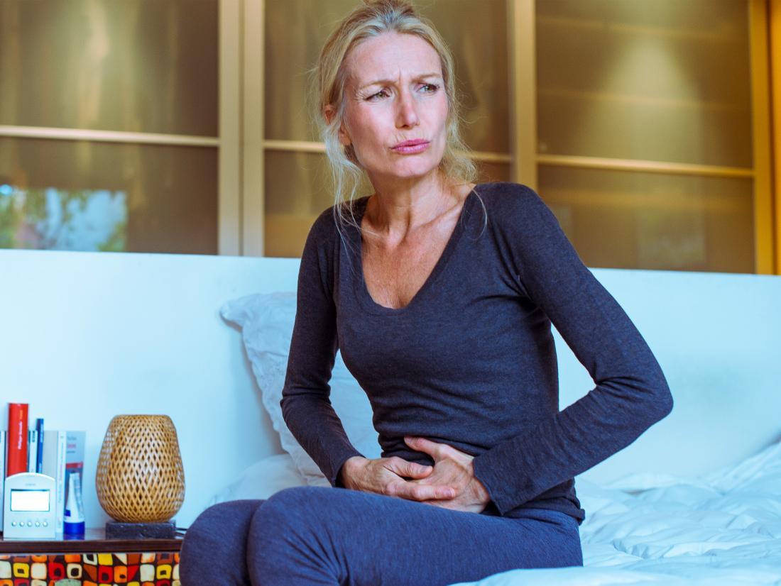 I woman sat on her bed feeling ill with either a Sour stomach or crohn's