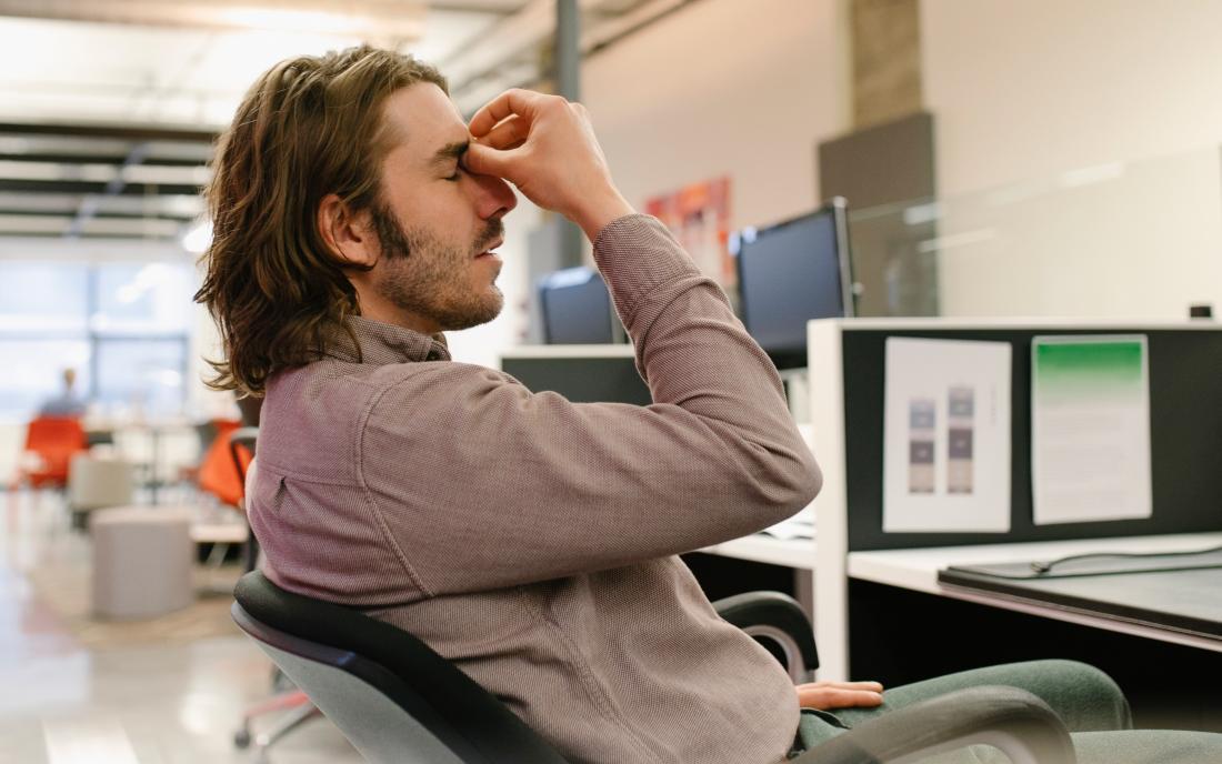 a man experiencing positional headache whilst sat on a chair as at a desk. 