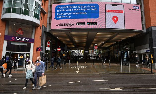 Shoppers pass beneath an electronic sign promoting the NHS Covi-19 app, outside the Arndale Centre in