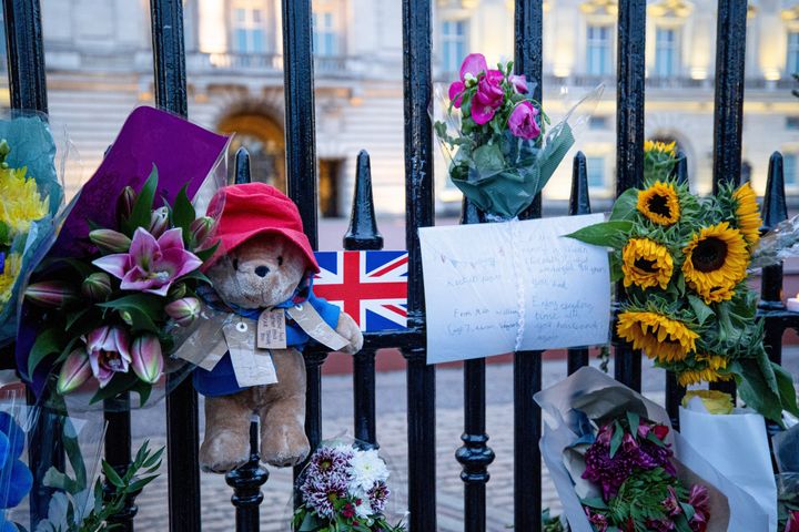 A Paddington bear with messages and flowers hangs at the gate of Buckingham Palace in London.