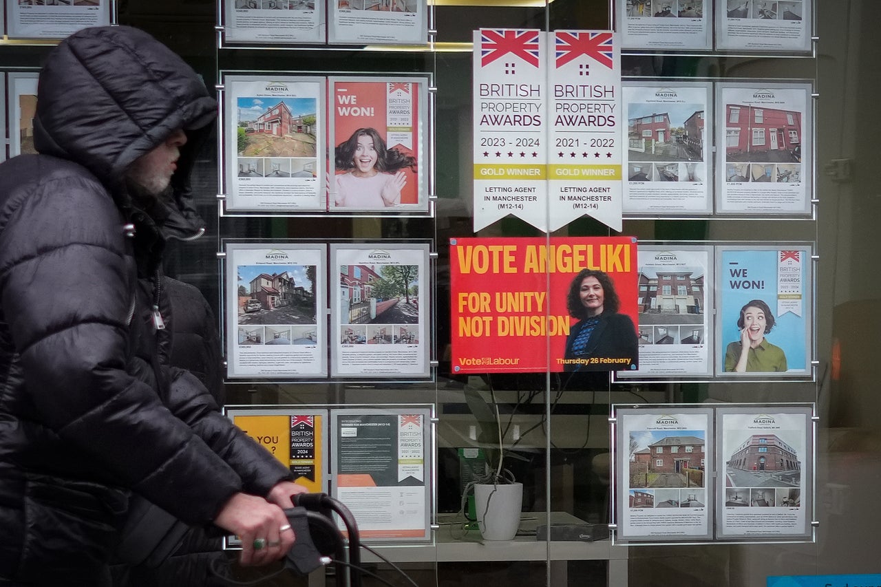 A man walks past a campaign poster for labour candidate Angeliki Stogia in an estate agents window in Longsight on February 11, 2026 in Manchester, United Kingdom.