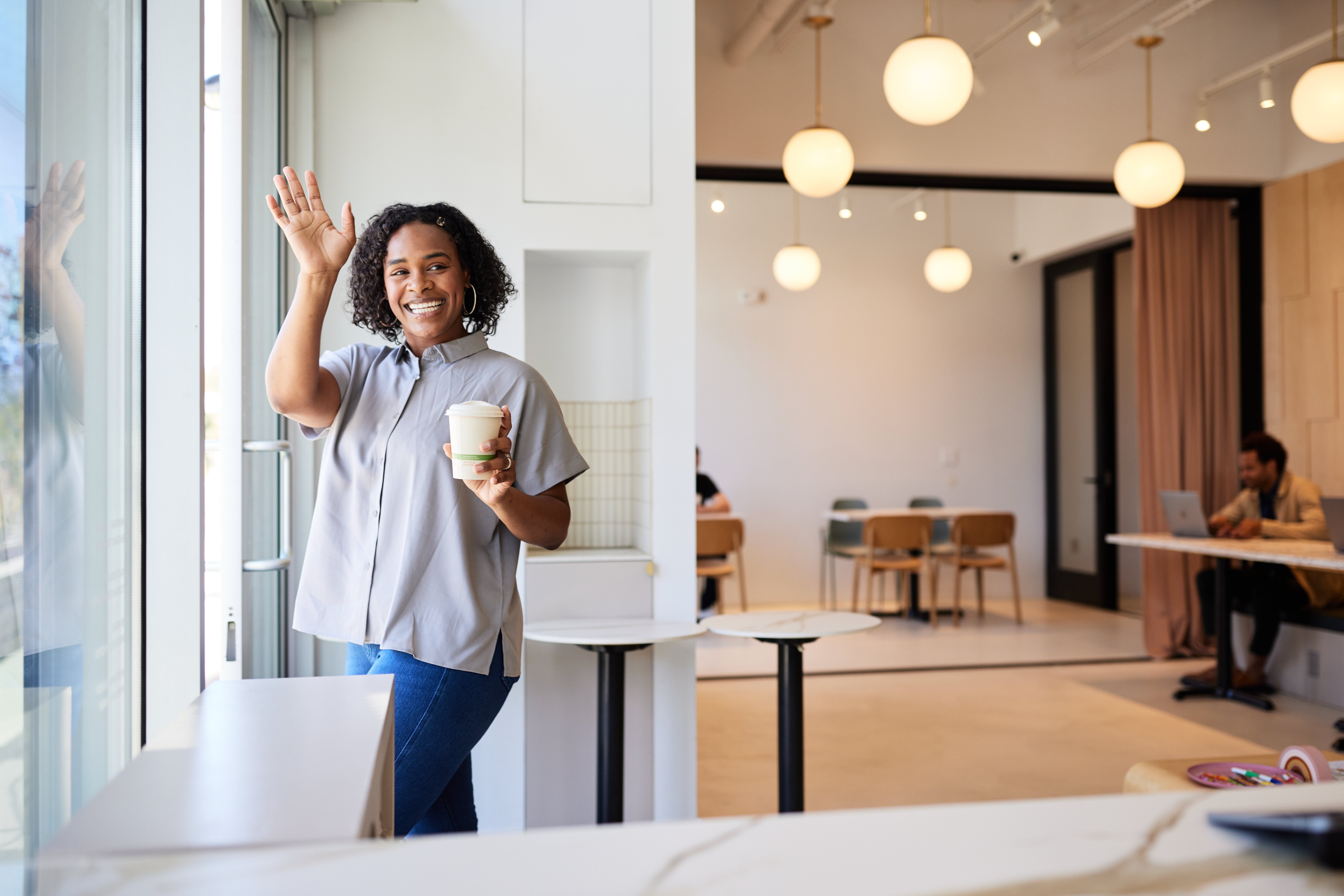 Happy woman with disposable coffee cup waving while leaving cafe