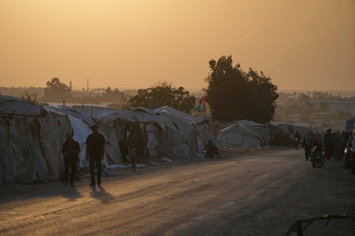Palestinians walk along a road lined with tents sheltering displaced people in Deir al-Balah, Gaza Strip, Thursday, Oct. 22, 2026.